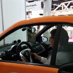 man sieht eine Frau am Steuer durch das Seitenfenster eines orangen, kleinen Autos.